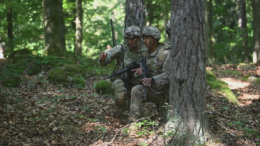 Two soldiers in tactical gear using tree cover during an electronic warfare field exercise